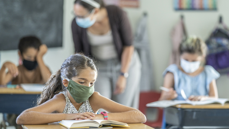 aluna de máscara na sala de aulas da escola com a professora e outros alunos em plano de fundo